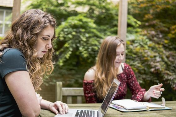 Two 波胆网站 students sit outside at a bistro table studying independently on their laptops. 